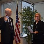 Tall man being sworn in by a woman in front of American flag